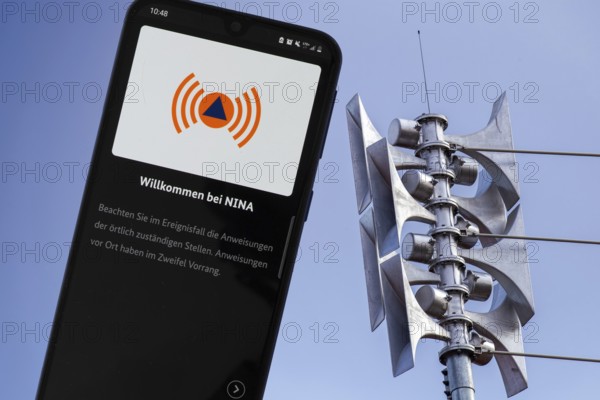 (Photomontage) Close-up of a siren at a school, next to it the open warning app NINA on a smartphone