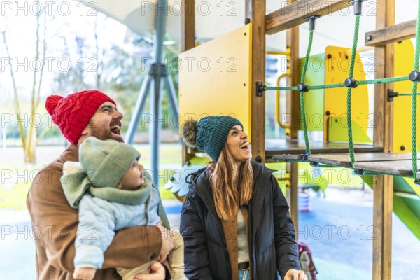 Cheerful parents and their baby are enjoying a playful day at the playground during wintertime