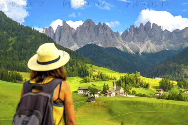 Woman with a backpack enjoying the serene summer landscape of santa maddalena village in val di funes, dolomites, italy
