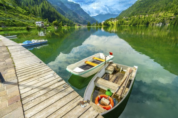 Wooden pier with boats reflecting in the emerald waters of alleghe lake with the dolomites in the background, italy