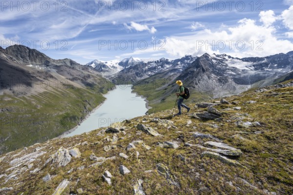 Mountaineer on the summit of Mont de la Blana, view of a blue mountain lake, Lac des Dix reservoir, behind mountain peak Mont Blanc de Cheilon with glacier, Hérménence, Valais Alps, Valais, Switzerland, Europe