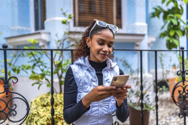 Urban young african american woman using phone sitting in the street next to a colorful building