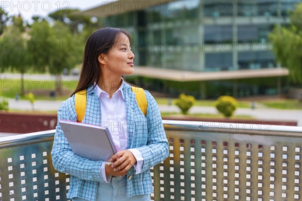 Three quarter length portrait of a beauty female chinese student looking away distracted standing in the university campus