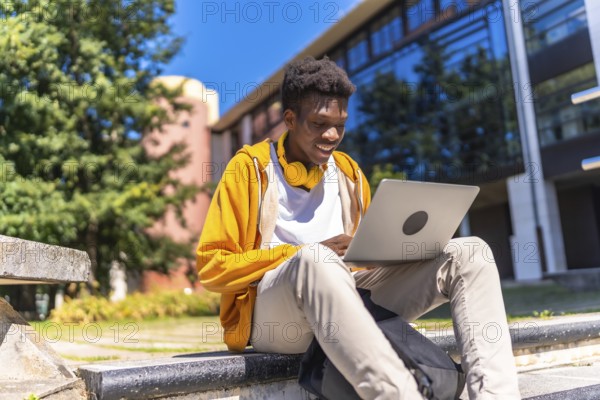 African man sitting at staircases on the university campus studying using laptop