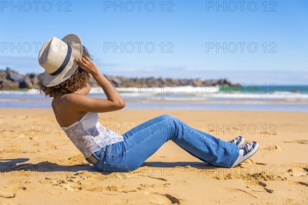 Side view of an unrecognzizable latin woman in summer denim clothes sitting on a beach gazing the ocean