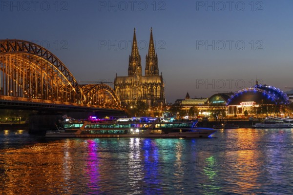 Cologne Cathedral, has been shining in new light since Easter 2025, the old metal halide lamps have been replaced by over 700 modern LED lamps, reducing energy consumption by around four-fifths, significantly improving the quality of light and greatly reducing light emissions, 12 KM of new cables were laid for this, KD Party Schiff, Hohenzollernbrücke, railway bridge over the Rhine, North Rhine-Westphalia, Germany, Europe