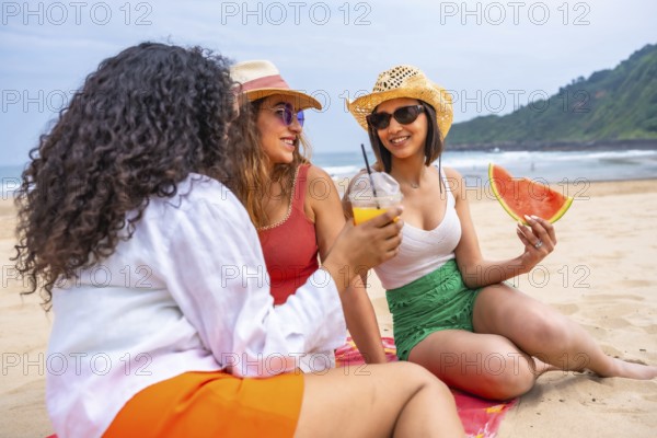 Multiethnic female friends enjoying summer on the beach on vacation, outdoors talking sitting on the sand