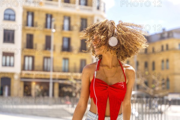Latin beauty young woman with curly hair dancing listening to music outdoors in the city