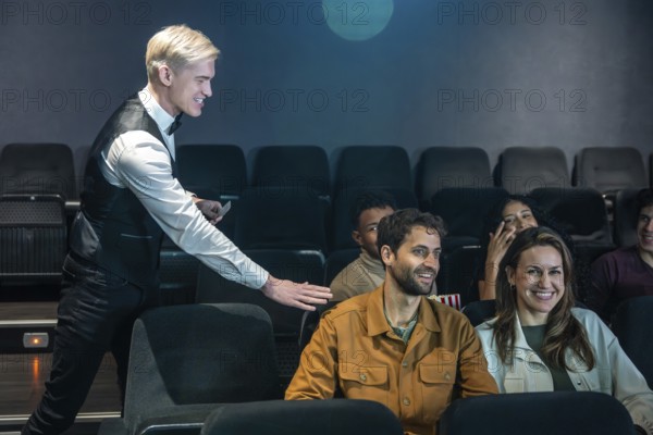 Movie theater usher guiding spectators to their seats and checking tickets, ensuring a smooth movie going experience for audience members