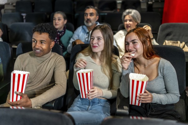 Group of friends watching a film at the movie theatre, eating popcorn and enjoying their leisure time