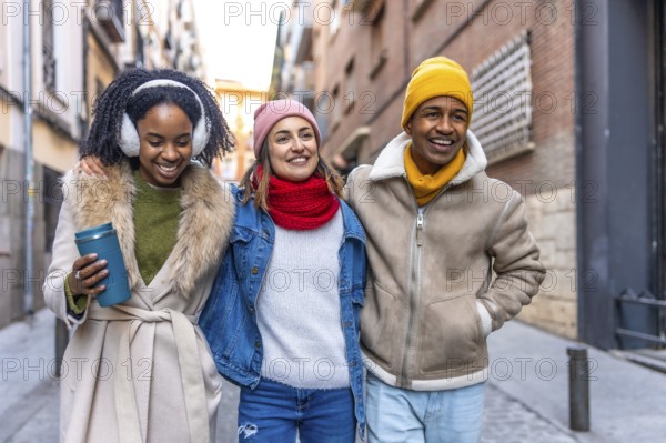 Happy multi ethnic friends are enjoying a winter day together, walking arm in arm through a city street