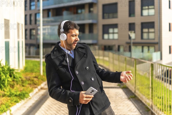 Adult caucasian businessman in casual winter clothes dancing while listening to music with mobile phone and headphones in the city