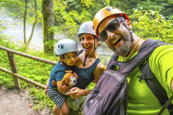 Happy family wearing helmets taking a selfie while hiking on a trail next to a river in vintgar gorge, bled, slovenia
