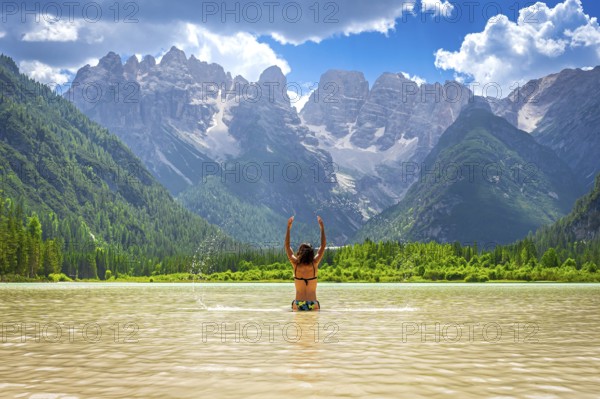 Tourist raising arms in the durrensee lake, enjoying summer holidays in the dolomites, italy