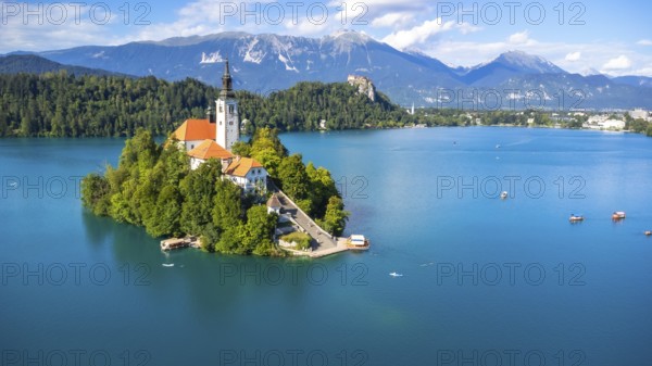 Aerial view of lake bled island with pilgrimage church of the assumption of maria on a sunny summer day with julian alps and bled castle in the background