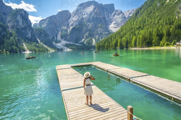 Tourist admiring the breathtaking landscape of lake braies, with its crystal clear turquoise waters nestled among majestic mountains and lush forests in the dolomites, italy