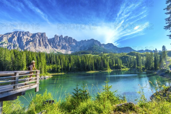 Female tourist admiring the stunning turquoise waters of lake carezza with the latemar mountain range in the background, dolomites, italy