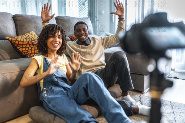 Two influencers happily waving at the camera while recording a video blog from their cozy living room, sharing their lives online