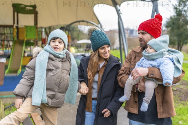 Happy family enjoying a delightful winter day at the playground, bundled up in warm clothes, sharing smiles and laughter together