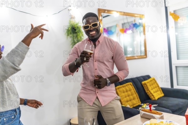 African man with pink t-shirt and sunglasses smiling drinking beer and dancing enjoying a home party with friends