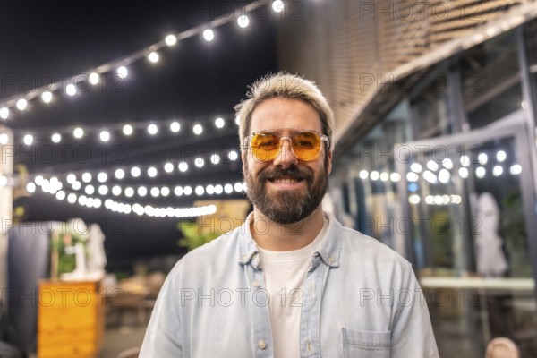 Hipster caucasian man with modern sunglasses smiling in a bar terrace at night