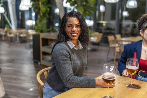 Latin woman smiling at camera sitting on a bar terrace with friends enjoying fresh beer