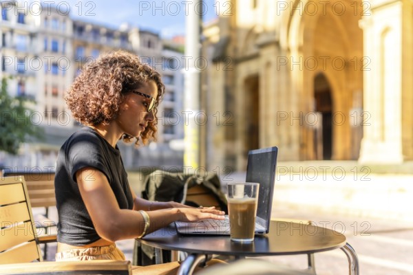 Arab young businesswoman working on remote in a sidewalk cafeteria in the main square of a city with ancient building on background