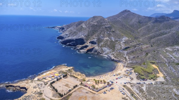 Aerial view of the stunning cala reona beach nestled between mountains in cabo de palos, spain, showcasing crystal clear turquoise waters and parked cars