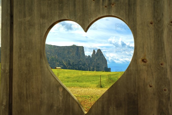 Breathtaking view of the italian dolomites, seen through a heart shaped opening in a wooden fence, showcasing the beauty of alpe di siusi