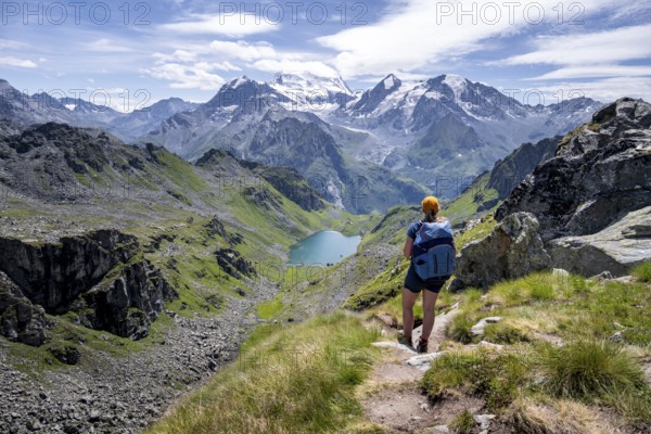 Hiker on hiking trail, mountain lake Lac de Louvie with glaciated summit of the Grand Combin, Val de Bagnes, Valais, Switzerland, Europe