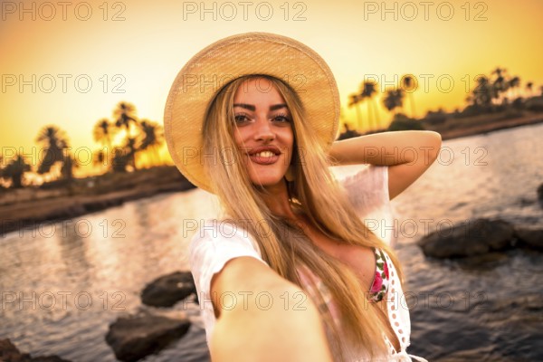 Personal point of view of a blonde woman smiling at camera while taking selfie during tropical sunset