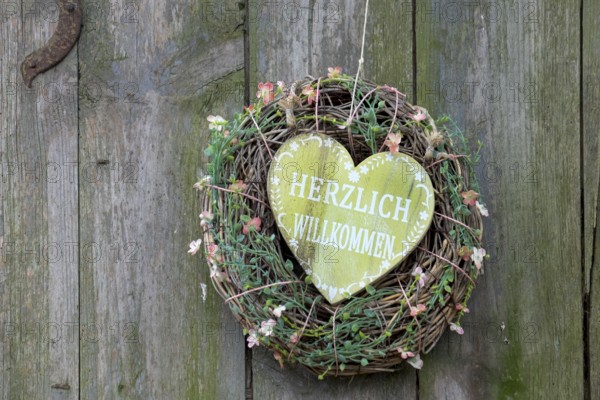 A heart-shaped welcome sign in a wreath with flowers, attached to a wooden surface, North Rhine-Westphalia, Germany, Europe