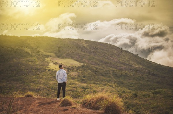 Rear view of a lonely man on top of a hill looking at the horizon. Back view of lonely man on a hill at sunset