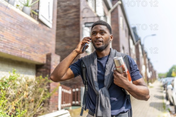 African entrepreneur talking to the mobile in the street holding a coffee hot thermos
