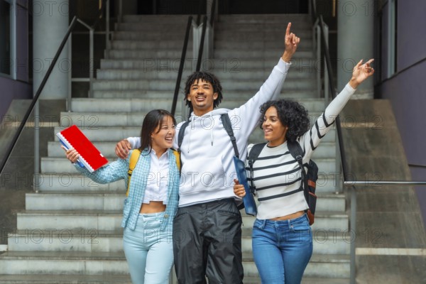 Three multi-ethnic students celebrating raising hands together outdoors the university