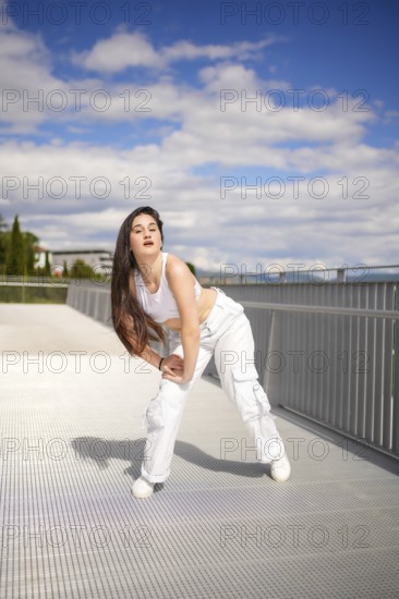 Vertical full length photo of a caucasian young female artist performing urban dance on a bridge