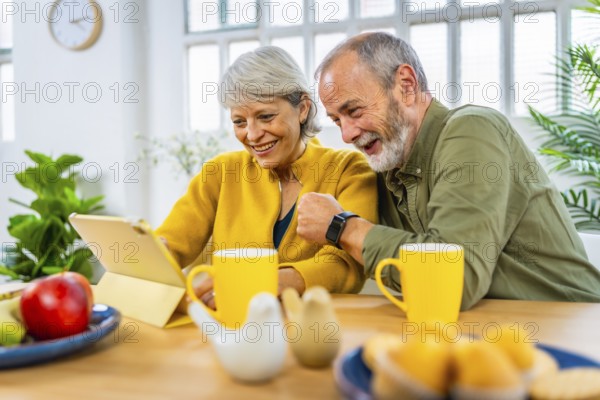 Happy married senior couple using tablet together while sharing breakfast at home