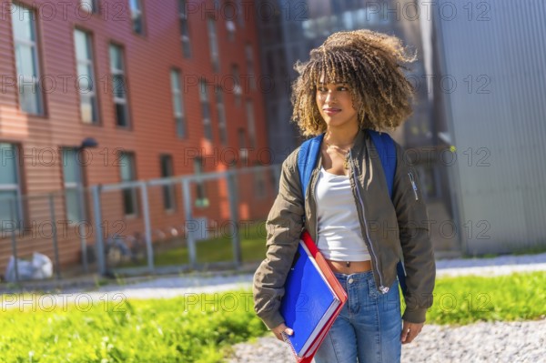 Confident latin young woman standing in the university campus looking away holding notebooks, folders and rucksack