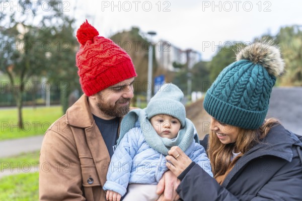 Smiling parents holding their baby wearing warm winter clothes and enjoying a winter day outdoors