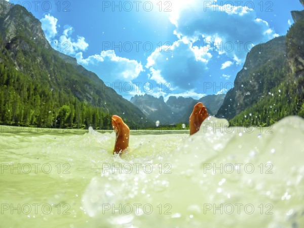 Feet of a tourist splashing in the turquoise water of lago di landro or durrensee lake, with the dolomites mountains in the background, in summer, italy