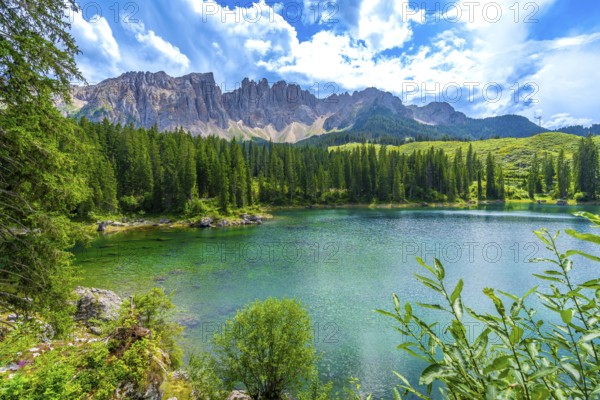 Emerald waters of lake carezza reflecting latemar mountain range in the dolomites, italy, on a beautiful summer day