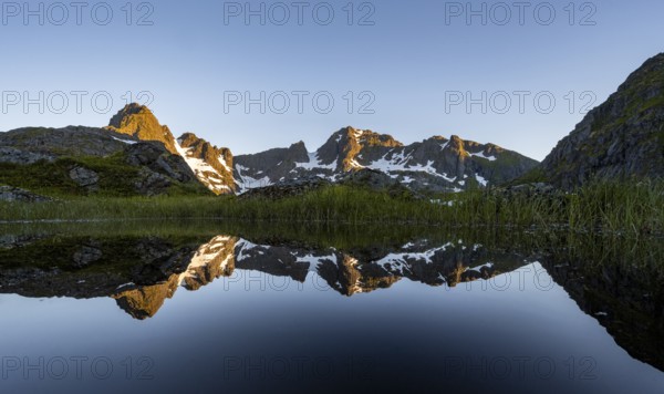 Rocky mountain peaks reflected in a small pond, mountain landscape with alpenglow at sunrise, at the Trollfjord Hytta, at the Trollfjord, Lofoten and Vesterålen, Nordland, Norway, Europe