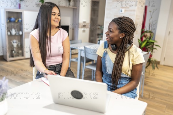 Two teenage girls are enjoying their time together at home, using a laptop and notebook to collaborate on their homework