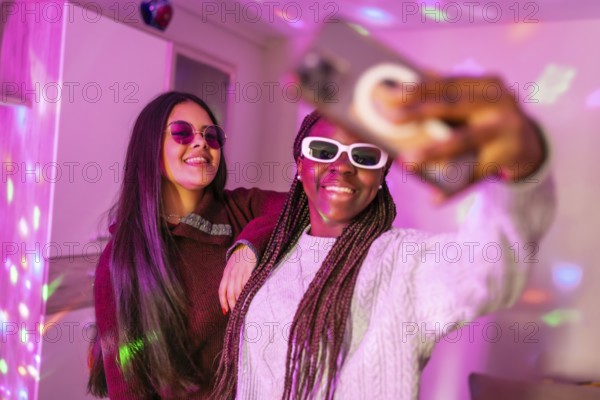 Two happy teenage girls taking a selfie with smartphone, enjoying a home party with disco lights