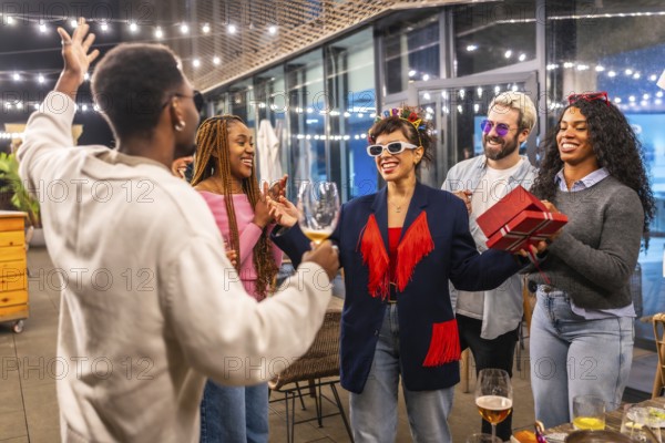 Multiracial friends celebrating surprise birthday party for a woman at night in the terrace of a bar