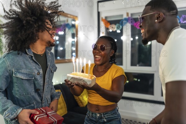 Young multiracial people surprising a friend with birthday cake and gift during night party at home