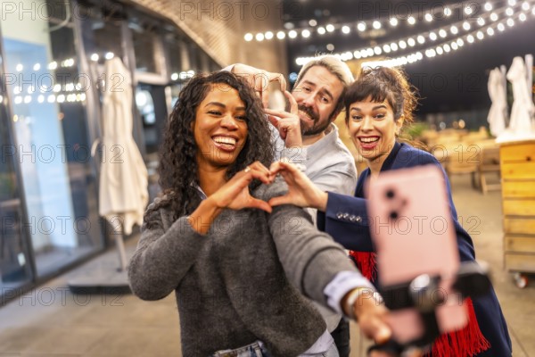 Multi-ethnic friends join hands gesturing heart shape while vlogging online in a night party