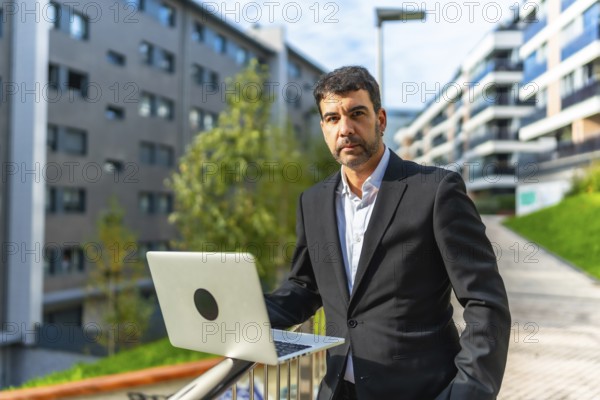 Portrait of a mature adult caucasian elegant and confident businessman using laptop standing in the city