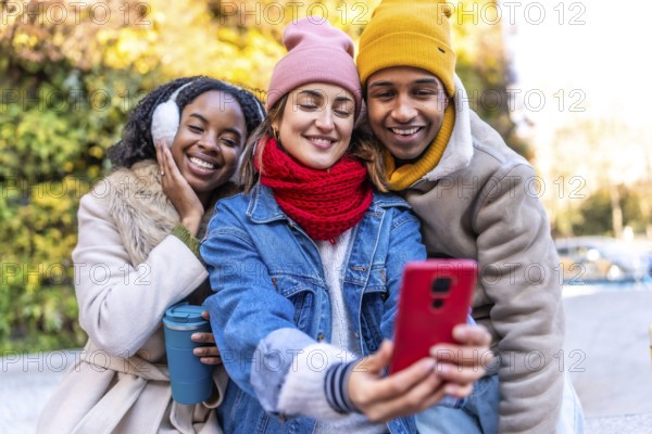 Multiracial young friends having fun together taking a selfie with smartphone in a winter city environment