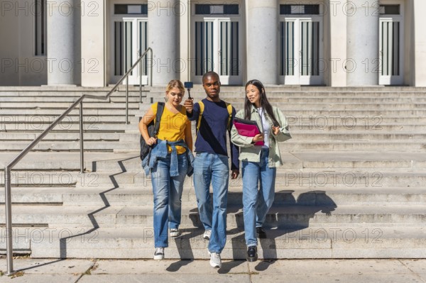 Three multi-ethnic university students walking down stairs recording online video blog with portable small camera
